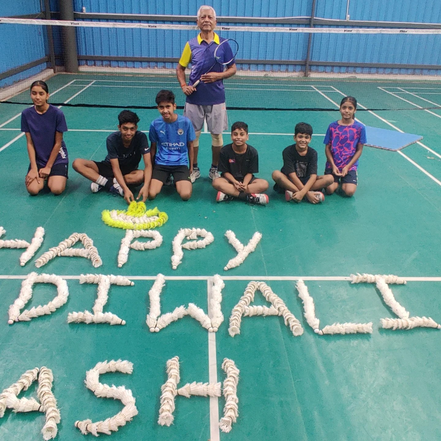 Happy Diwali spelled out in shuttlecocks on the court with young players